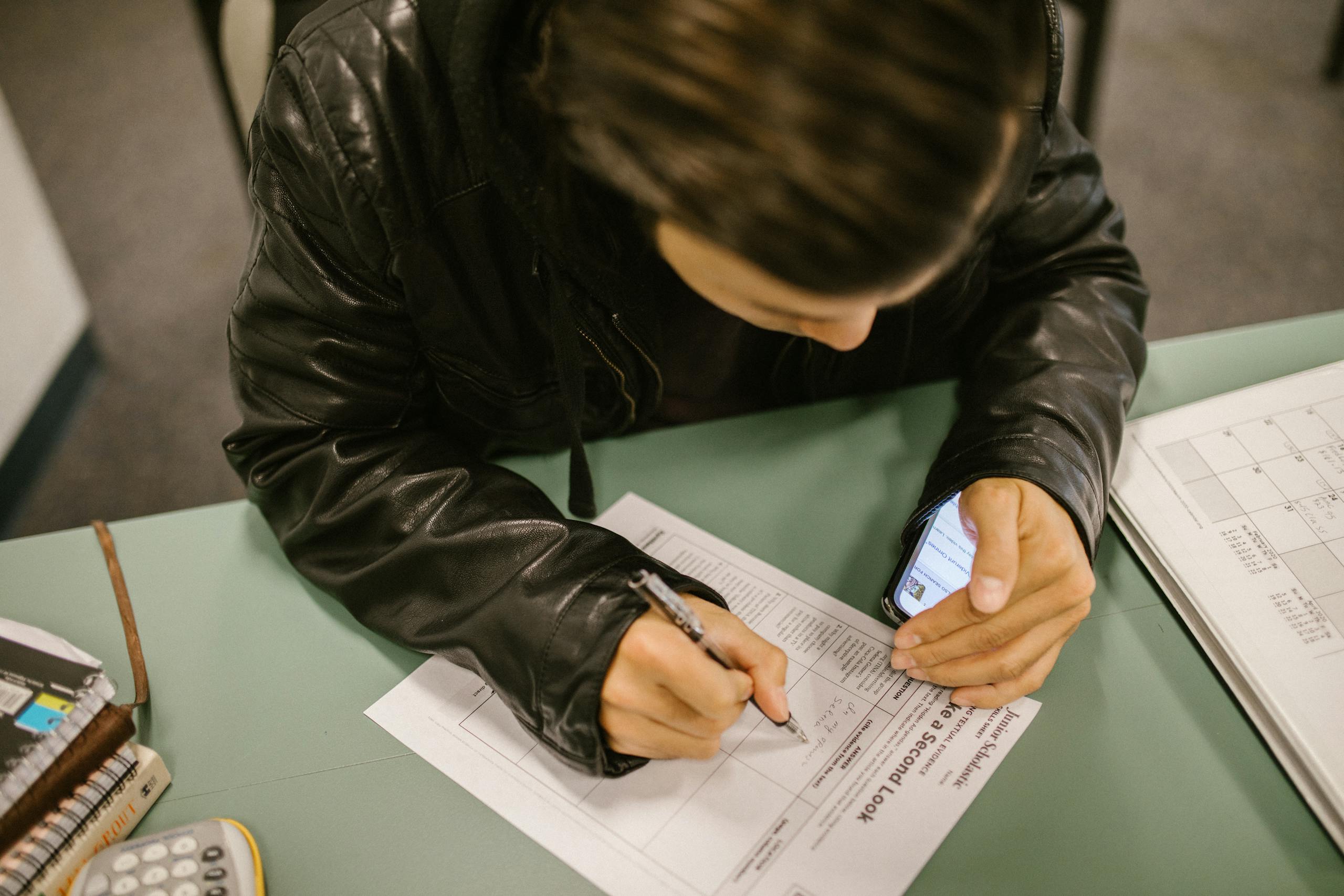 An overhead shot of a student using a smartphone to cheat during an exam in a classroom setting.